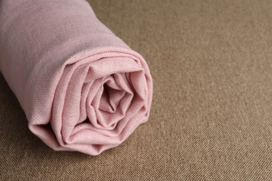 Rolled pink fabric on brown cloth, closeup. Space for text