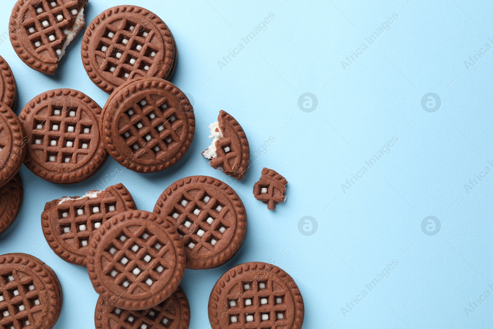 Photo of Tasty chocolate sandwich cookies with cream on light blue background, flat lay. Space for text