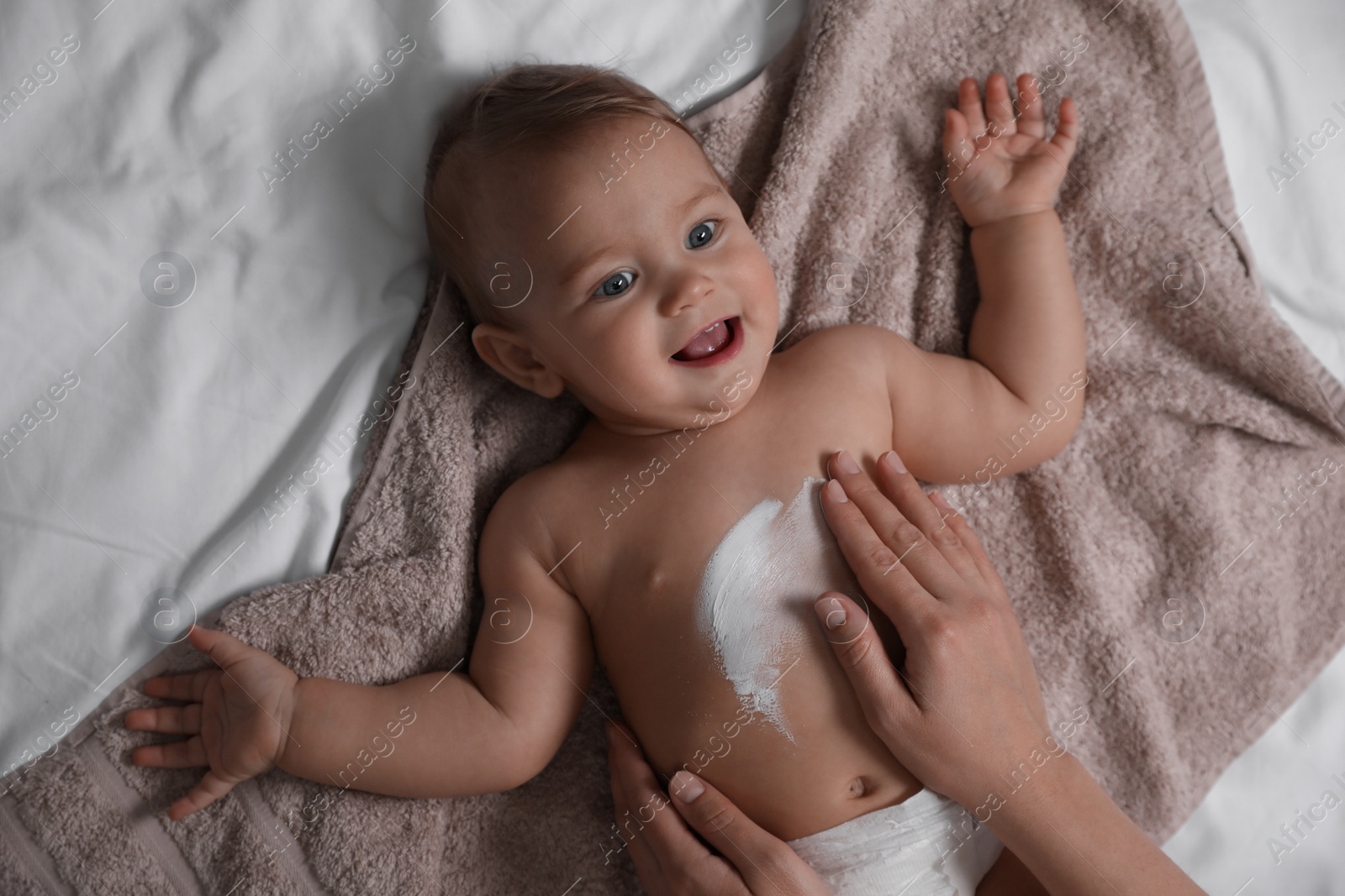 Photo of Mother applying moisturizing cream onto her little baby's skin on towel, closeup