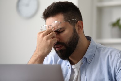 Photo of Man with glasses suffering from headache at workplace in office