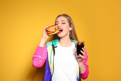 Pretty woman with tasty burger and cola on color background