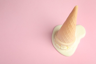 Photo of Melted vanilla ice cream in wafer cone on pink background, above view. Space for text