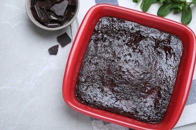 Photo of Delicious brownie in baking dish, pieces of chocolate and fresh mint on light grey table, flat lay