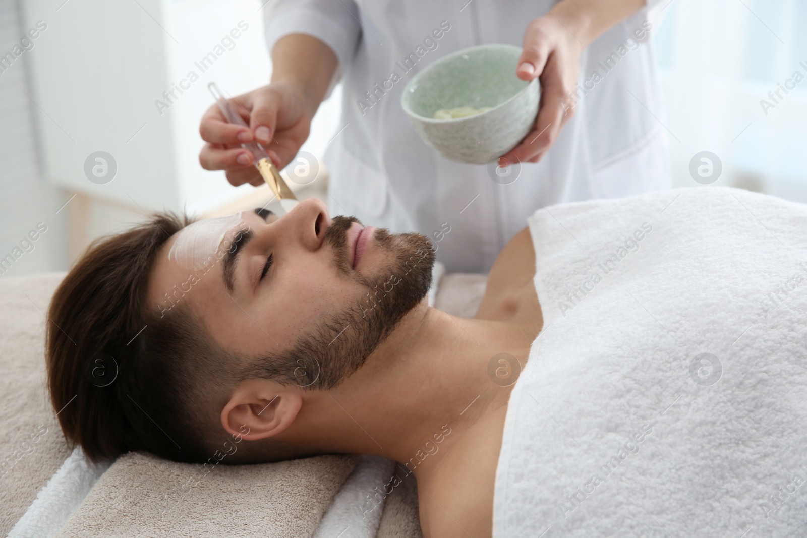 Photo of Cosmetologist applying mask on client's face in spa salon