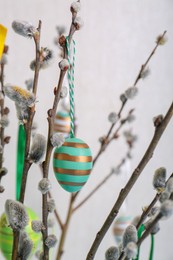 Photo of Beautiful willow branches with painted eggs on light blue grey background, closeup. Easter decor
