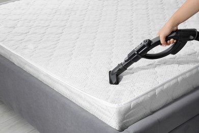 Photo of Woman disinfecting mattress with vacuum cleaner, closeup