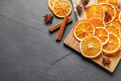Photo of Many dry orange slices and spices on black textured table, flat lay. Space for text