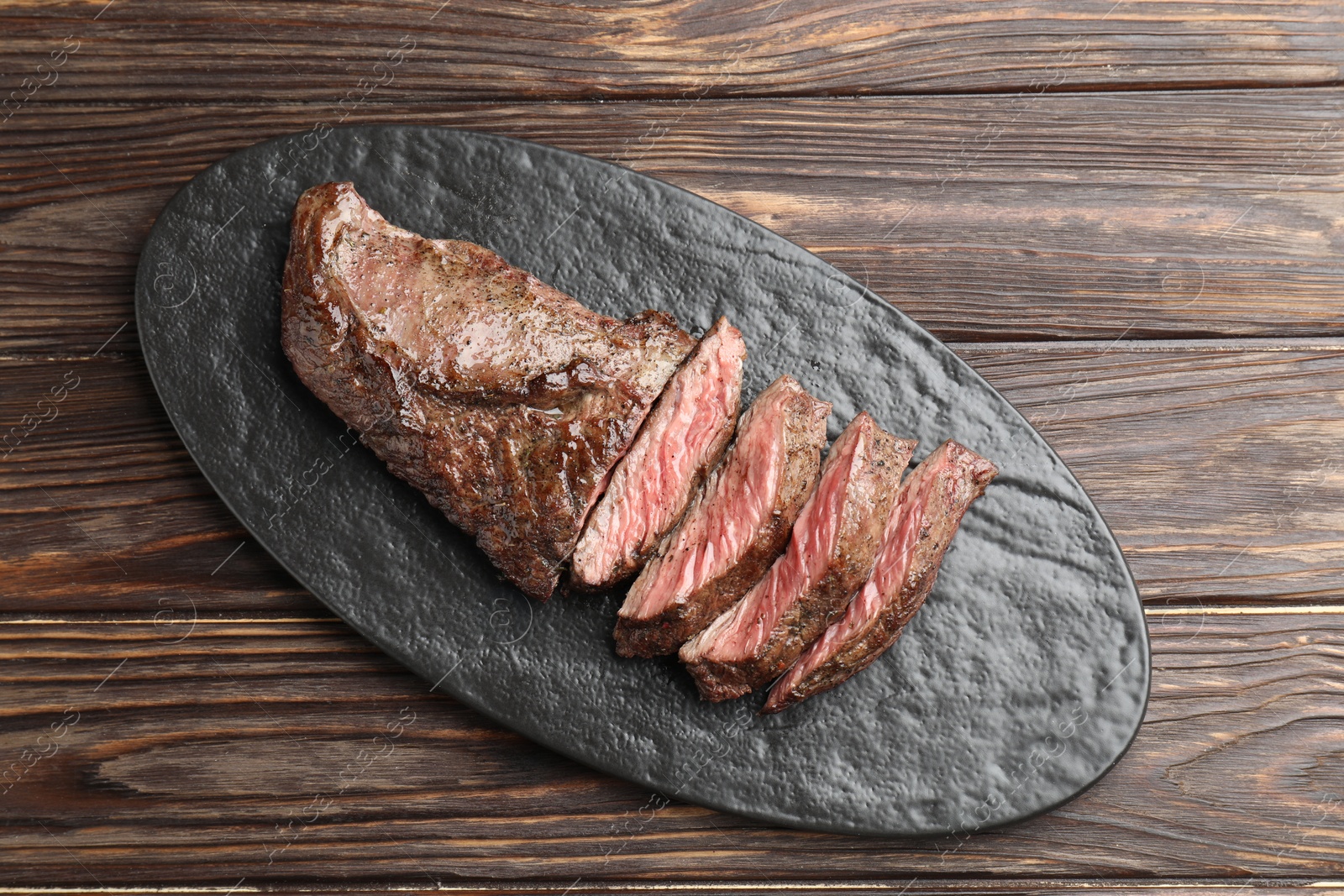 Photo of Pieces of delicious grilled beef meat on wooden table, top view