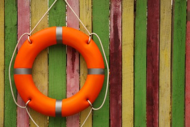 Photo of Orange lifebuoy hanging on color wooden fence, space for text. Rescue equipment
