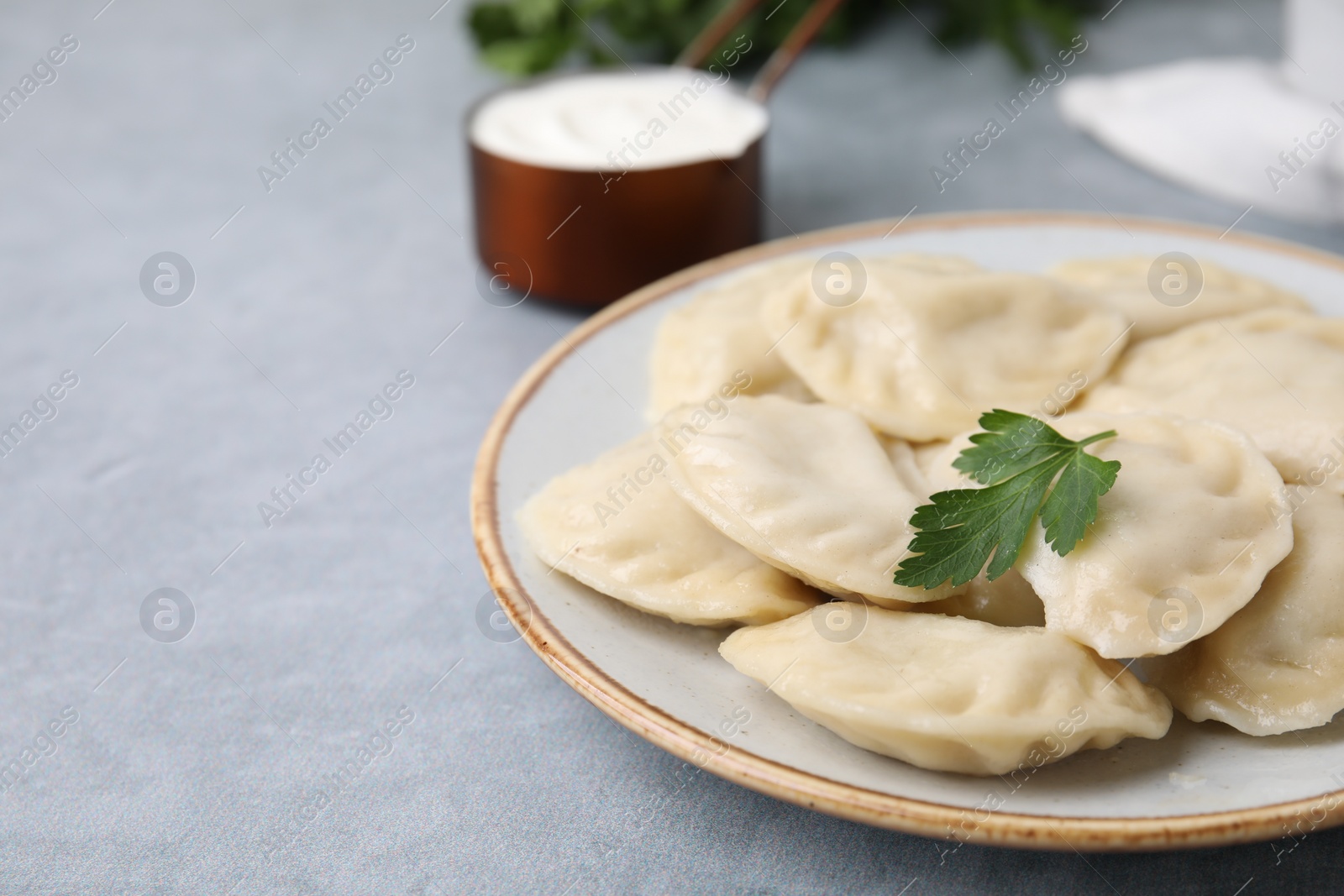 Photo of Delicious dumplings (varenyky) with tasty filling and parsley on light grey table, closeup. Space for text