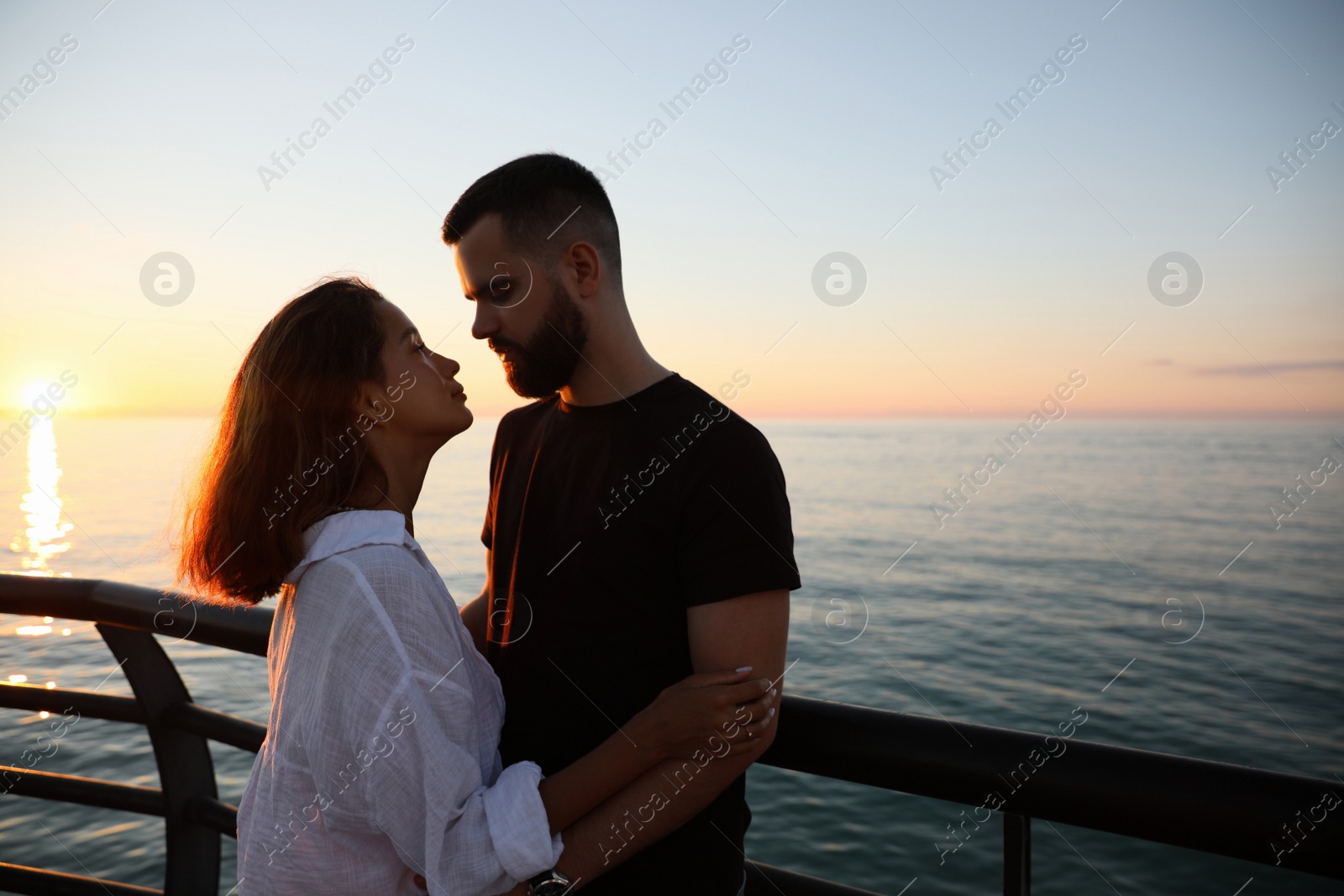 Photo of Happy young couple hugging on sea embankment at sunset