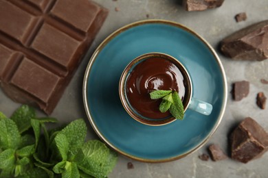 Photo of Cup of delicious hot chocolate, chunks and fresh mint on grey table, flat lay
