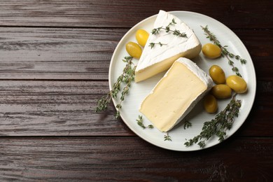 Photo of Plate with pieces of tasty camembert cheese, olives and rosemary on wooden table, top view. Space for text