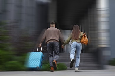 Being late. Young couple with suitcase running on city street, back view. Motion blur effect