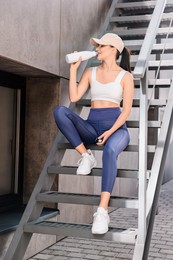 Photo of Beautiful woman in sportswear drinking from thermo bottle on stairs outdoors