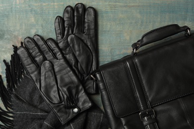 Photo of Stylish black leather gloves, bag and scarf on blue wooden table, flat lay