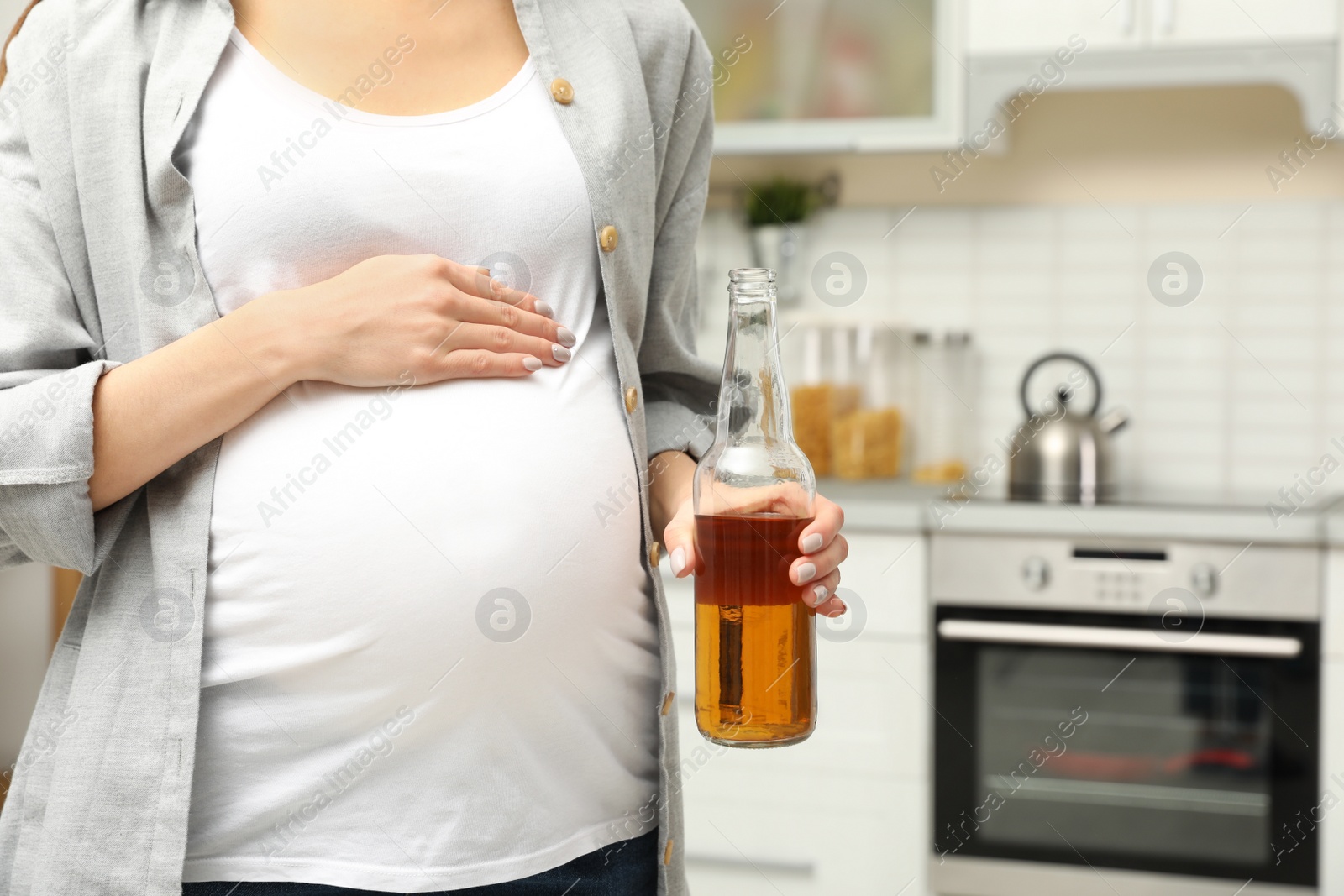 Photo of Future mother with bottle of alcohol drink in kitchen, closeup. Bad habits during pregnancy