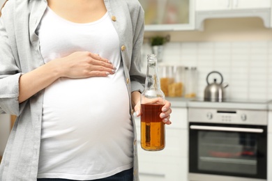 Photo of Future mother with bottle of alcohol drink in kitchen, closeup. Bad habits during pregnancy