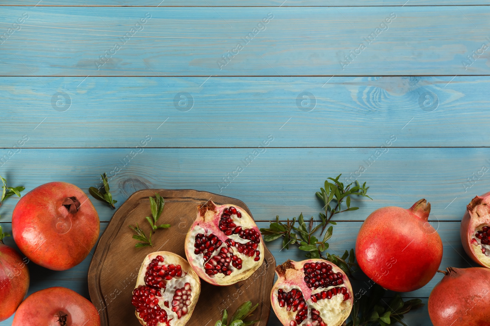 Photo of Flat lay composition with ripe pomegranates on light blue wooden table. Space for text