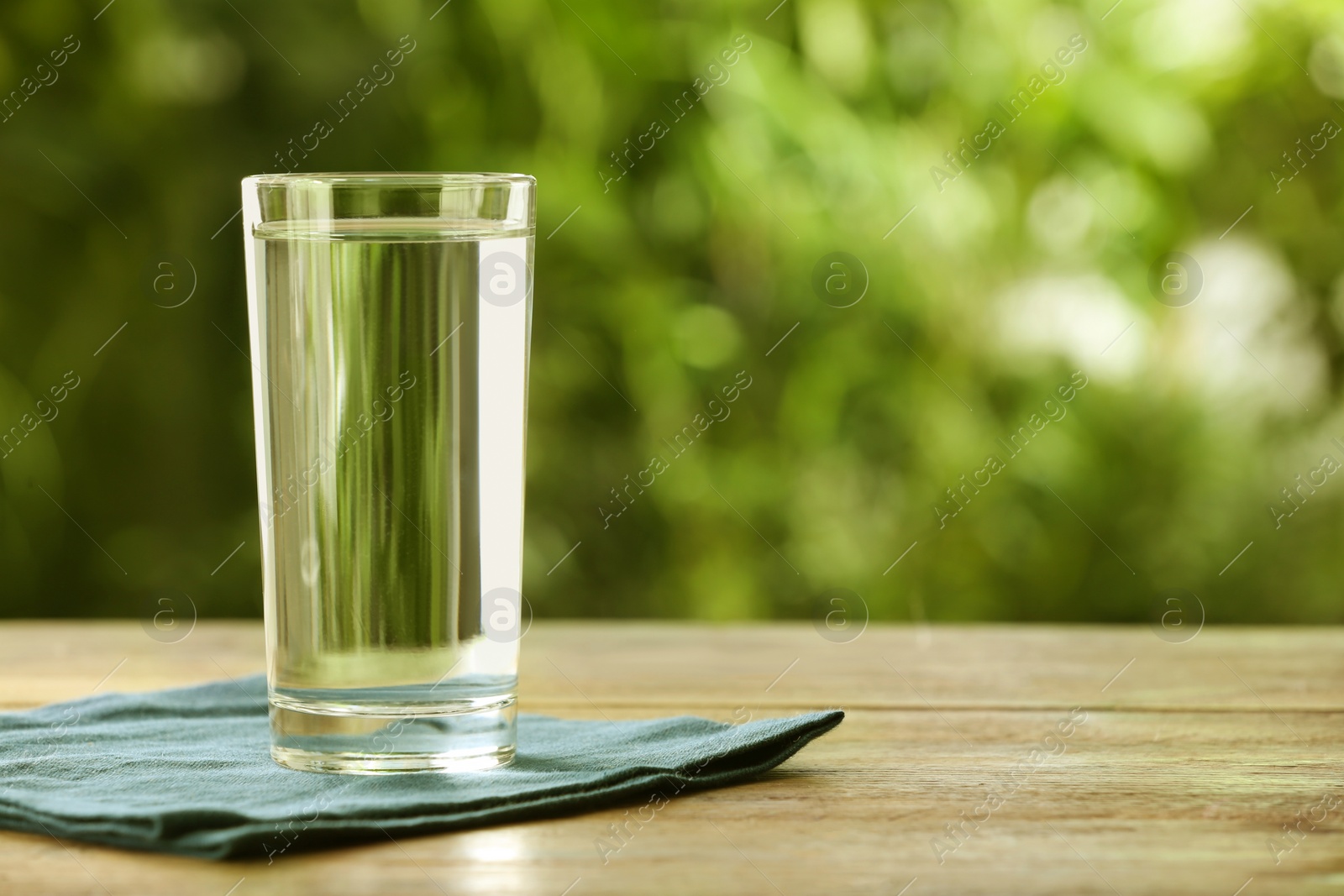 Photo of Glass of fresh water on wooden table outdoors, space for text