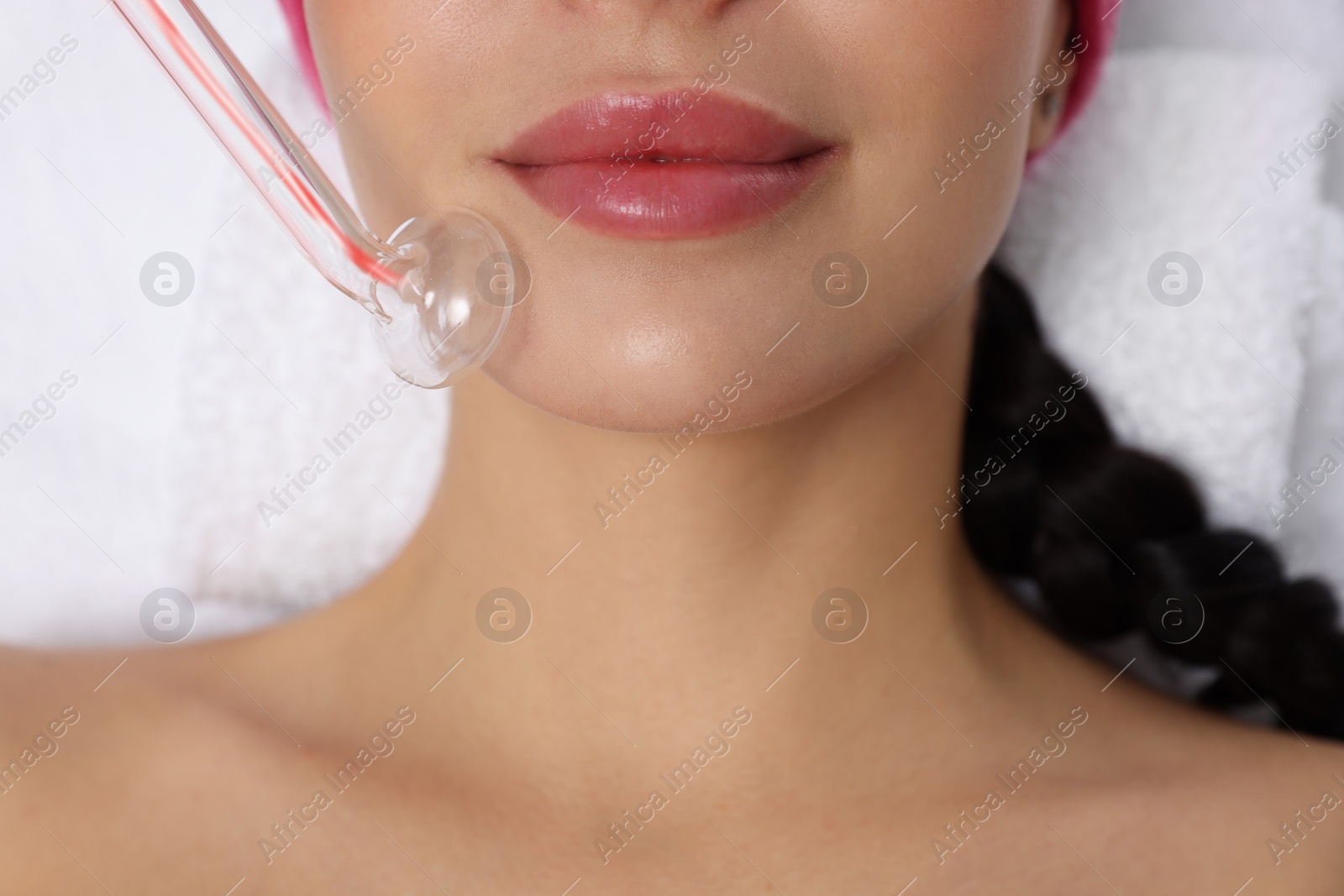 Photo of Young woman undergoing face rejuvenation procedure with darsonval in salon, closeup