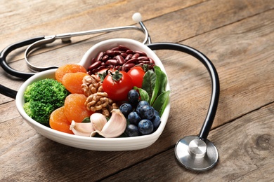 Photo of Bowl with heart-healthy diet products and stethoscope on wooden table. Space for text