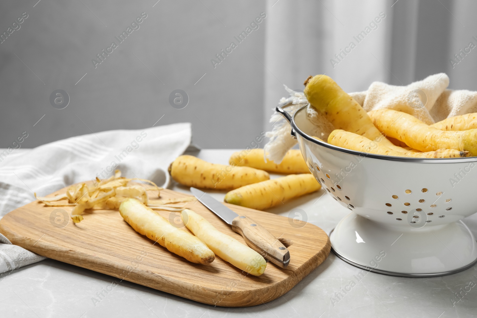 Photo of Raw white carrots, knife and cutting board on light grey marble table