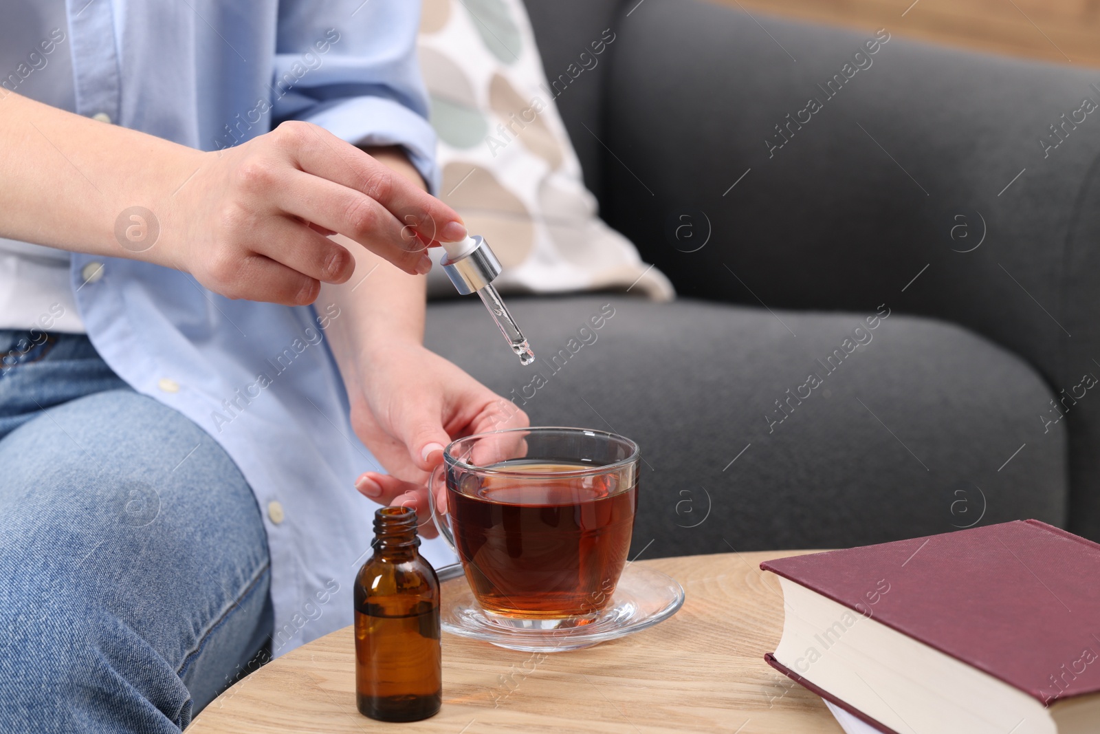 Photo of Woman dripping food supplement into cup of tea at wooden table indoors, closeup