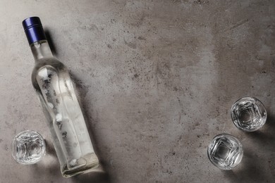 Photo of Bottle of vodka and shot glasses on grey table, flat lay. Space for text