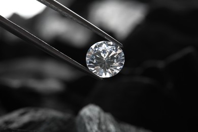 Photo of Tweezers with beautiful shiny diamond on dark background, closeup