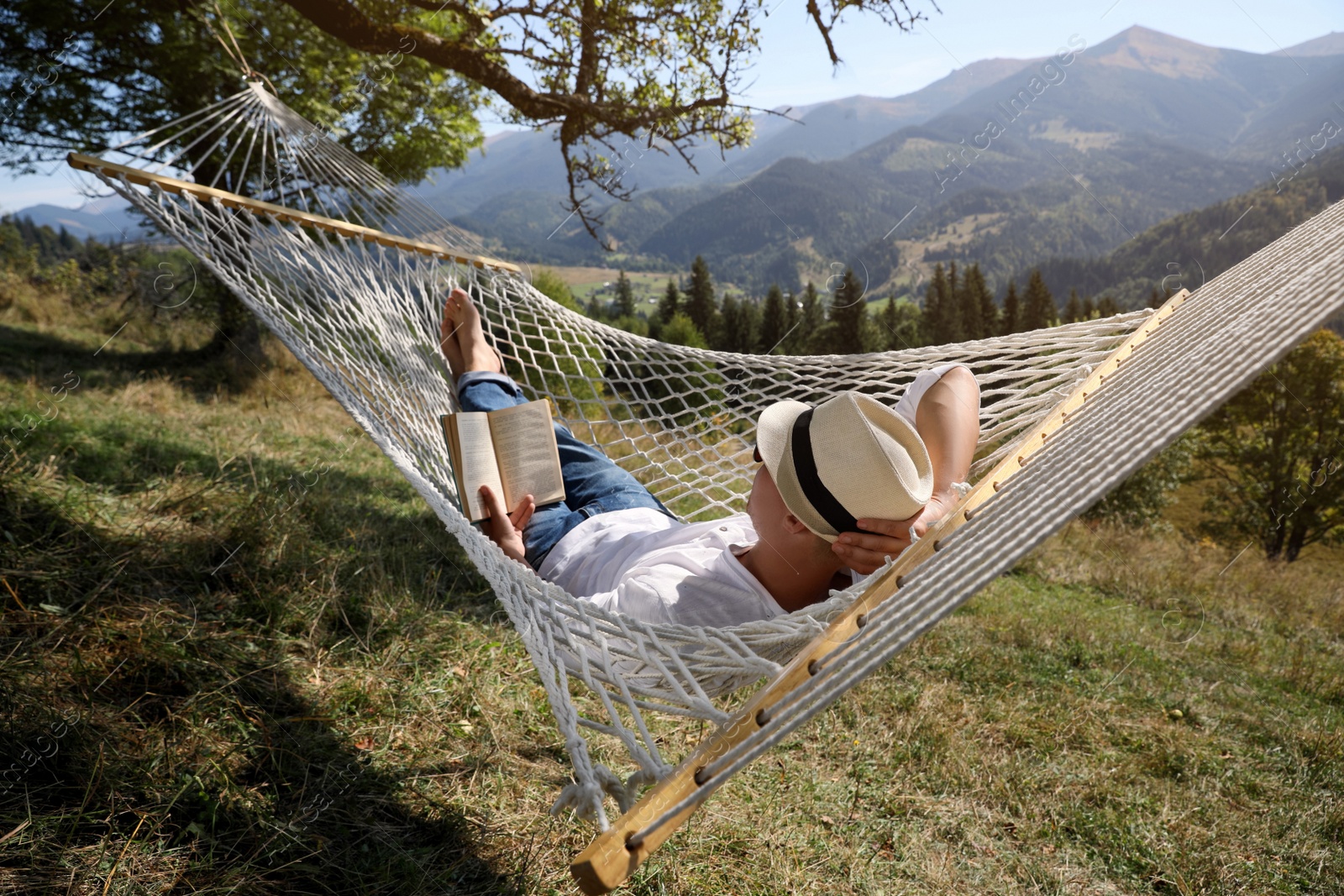 Photo of Young man reading book in hammock outdoors on sunny day