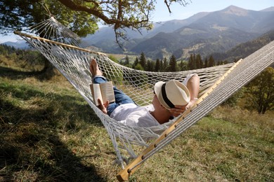 Young man reading book in hammock outdoors on sunny day