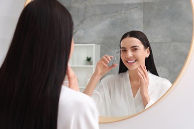 Photo of Beautiful young woman using eyelash curler near mirror in bathroom
