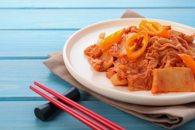 Photo of Plate of spicy cabbage kimchi with chili pepper and chopsticks on light blue wooden table, closeup