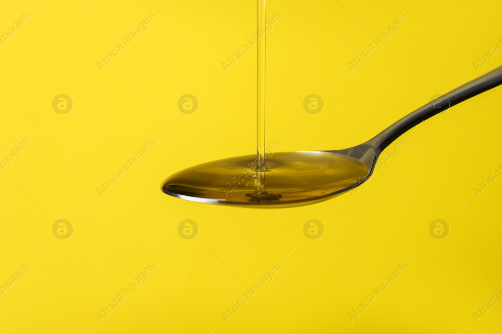 Photo of Pouring cooking oil into spoon on yellow background, closeup