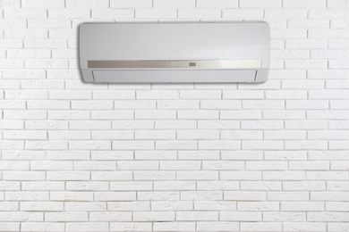 Modern air conditioner on white brick wall indoors