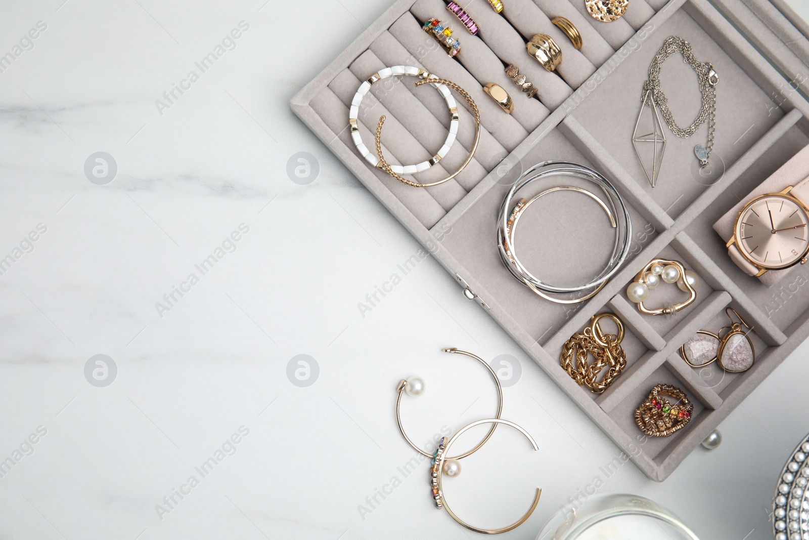 Photo of Elegant jewelry box with beautiful bijouterie on white marble table, flat lay. Space for text