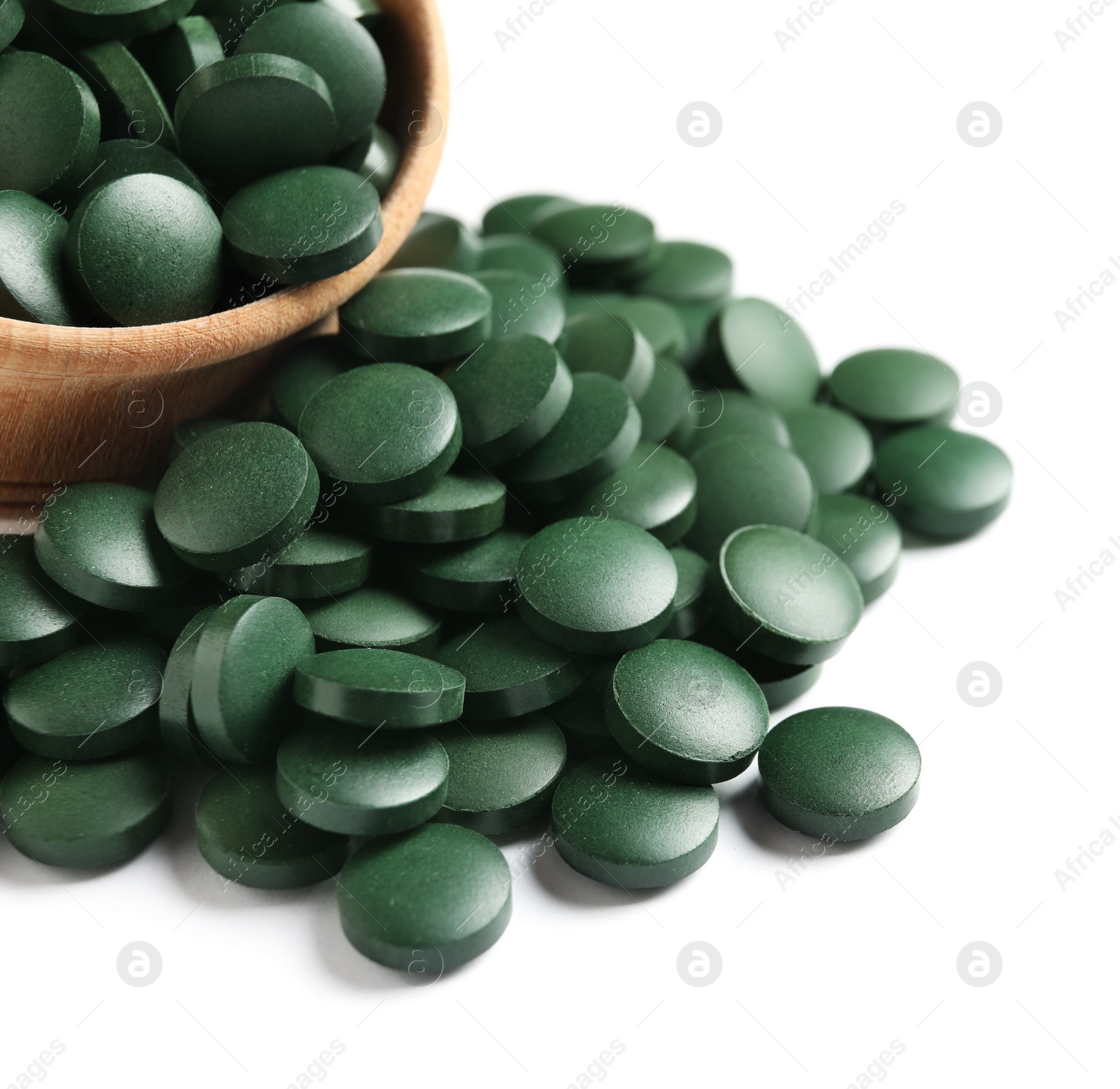 Photo of Wooden bowl with green spirulina pills on white background, closeup