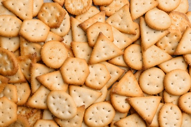 Many delicious crackers as background, top view