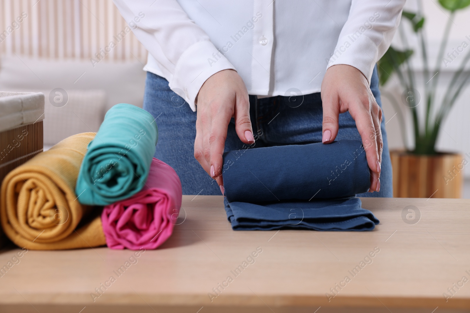 Photo of Woman rolling shirt at table in room, closeup. Organizing clothes