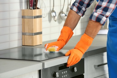 Photo of Man cleaning kitchen stove with sponge, closeup