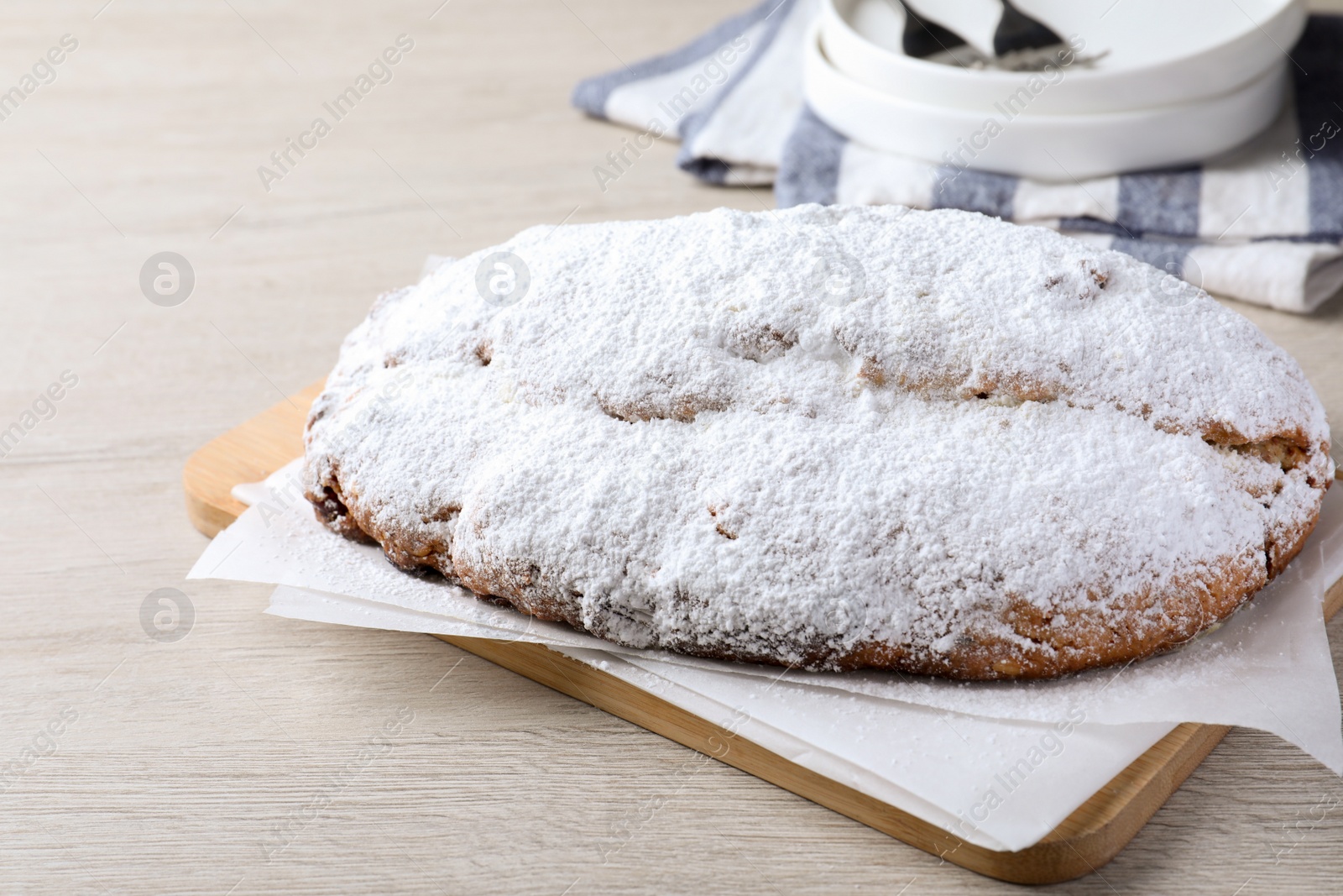 Photo of Delicious Stollen sprinkled with powdered sugar on wooden table