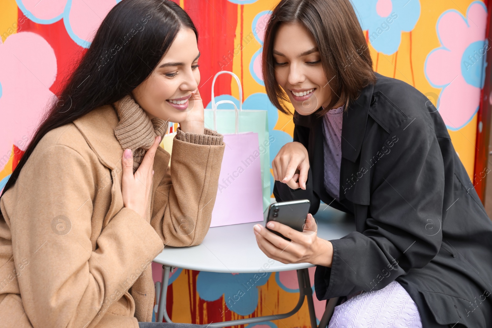 Photo of Special Promotion. Happy young women with shopping bags using smartphone in outdoor cafe