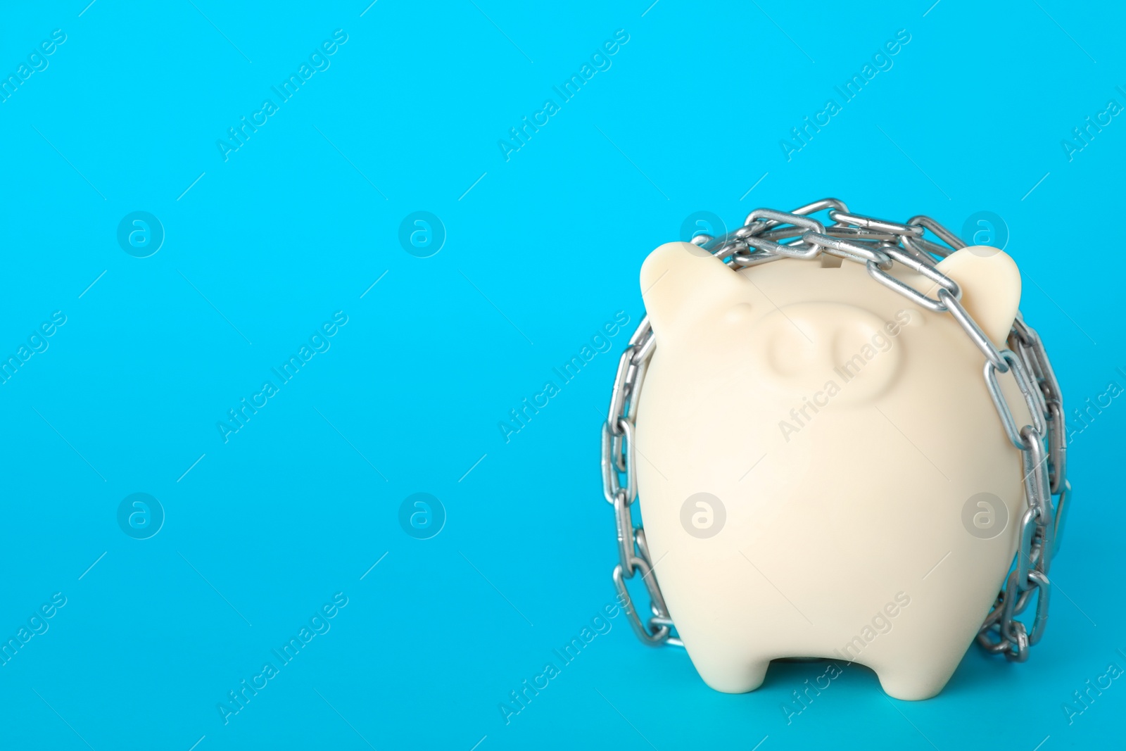 Photo of Piggy bank  with steel chain on light blue background, space for text. Money safety concept