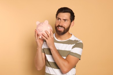 Happy man with ceramic piggy bank on beige background