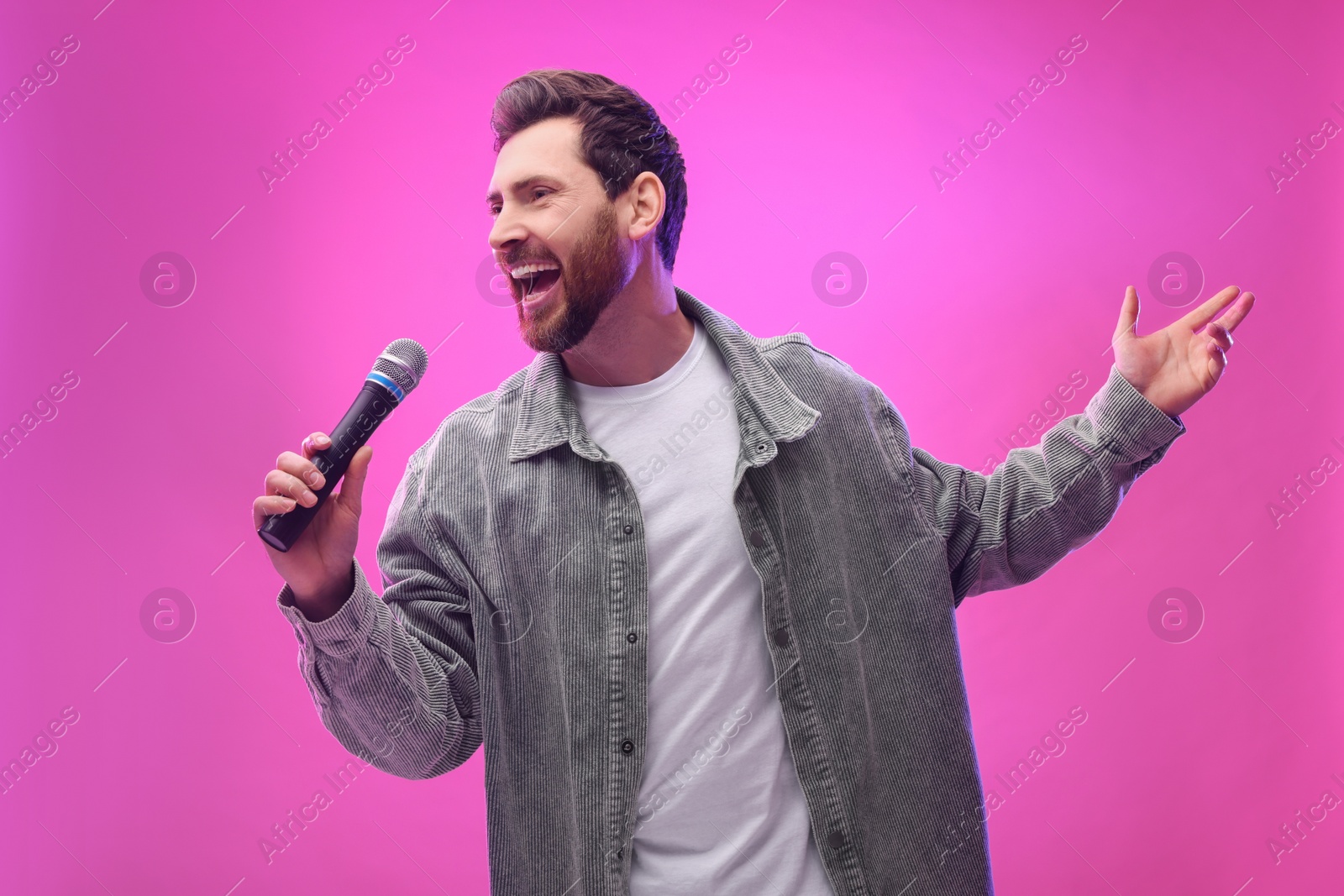 Photo of Handsome man with microphone singing on pink background