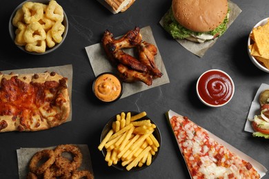 Burger, pizza and other fast food on black table, flat lay