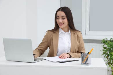 Young female intern working with laptop at table in office