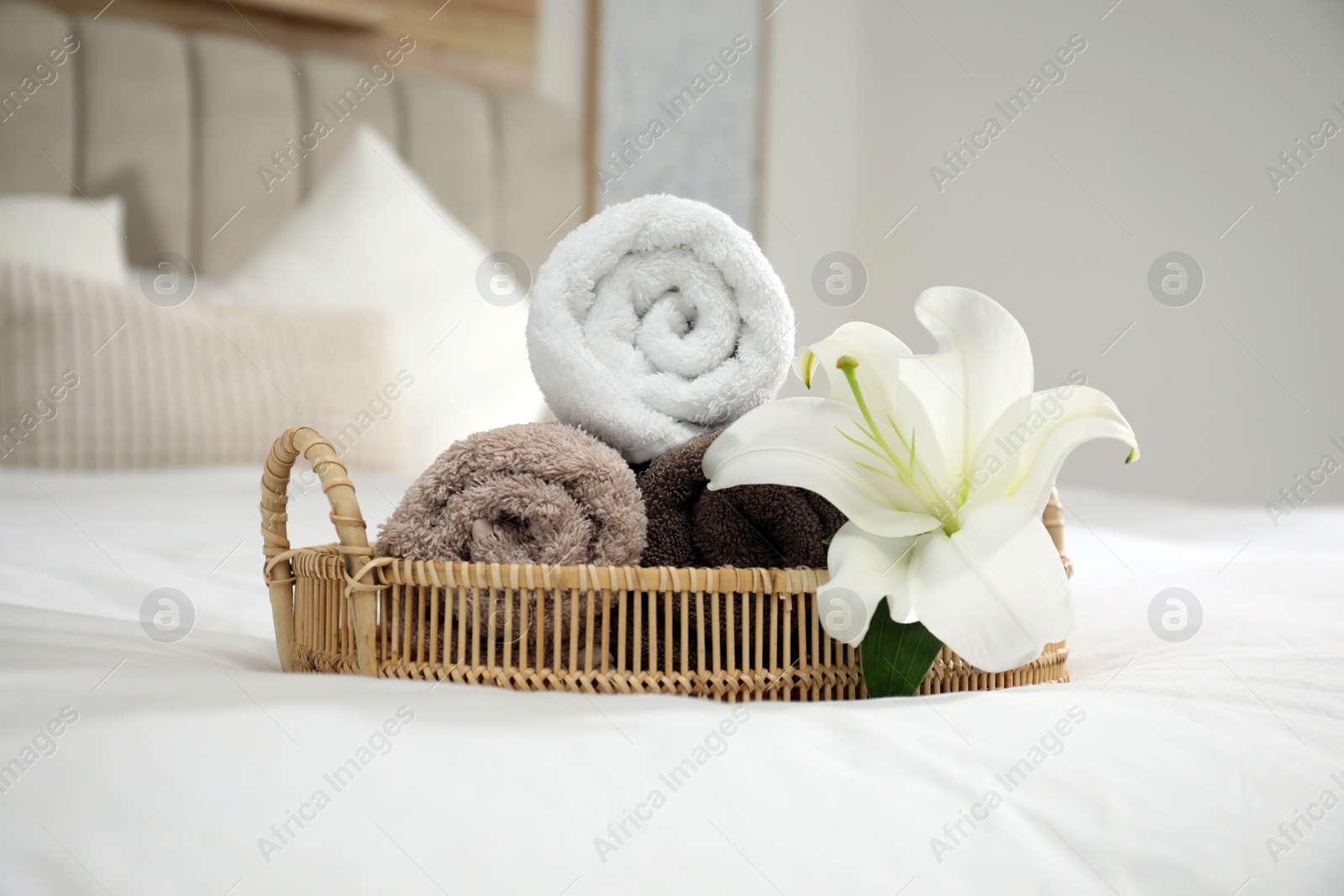 Photo of Rolled clean towels and flower on bed indoors