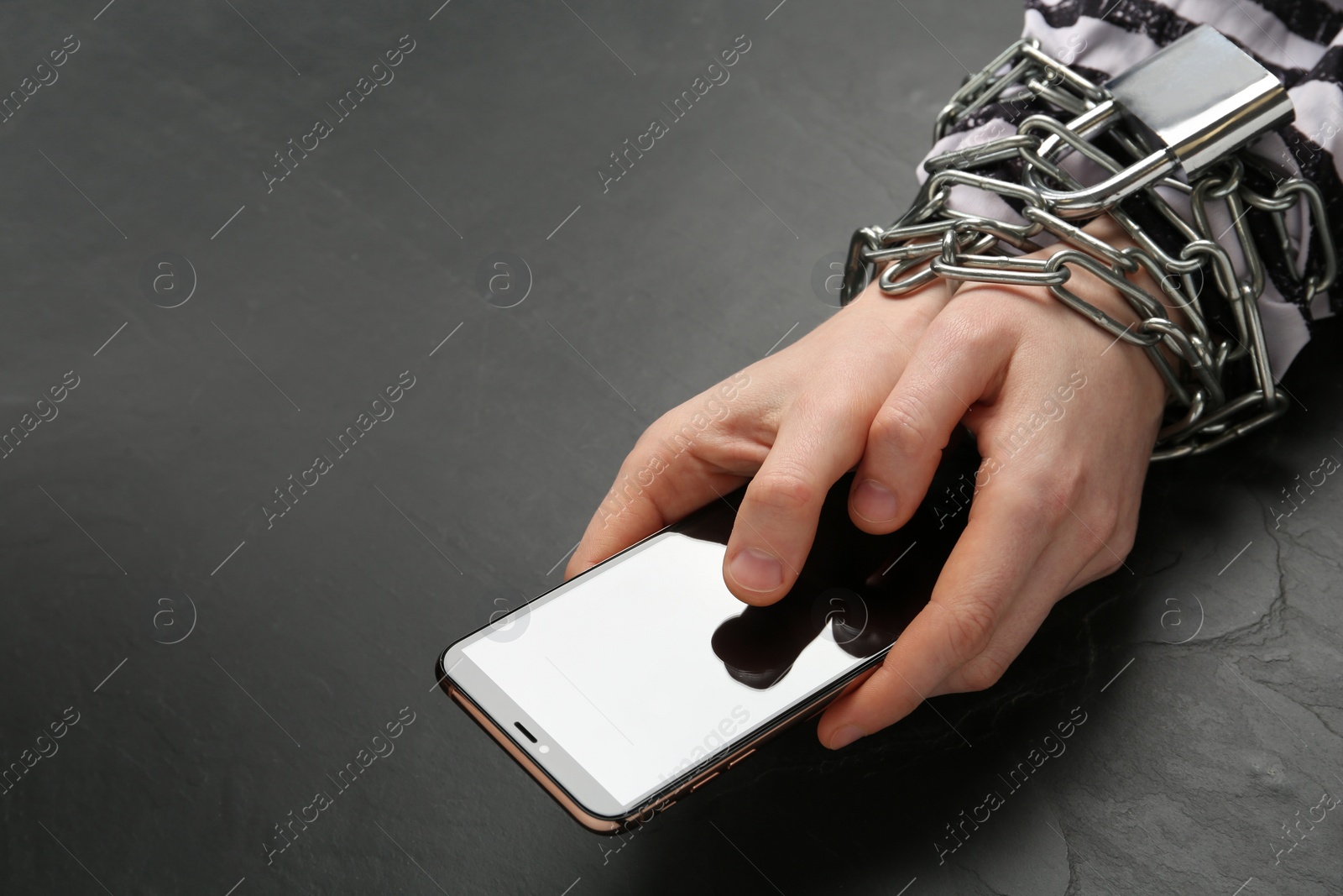 Photo of Prisoner holding smartphone in chained hands at black table, closeup. Internet addiction
